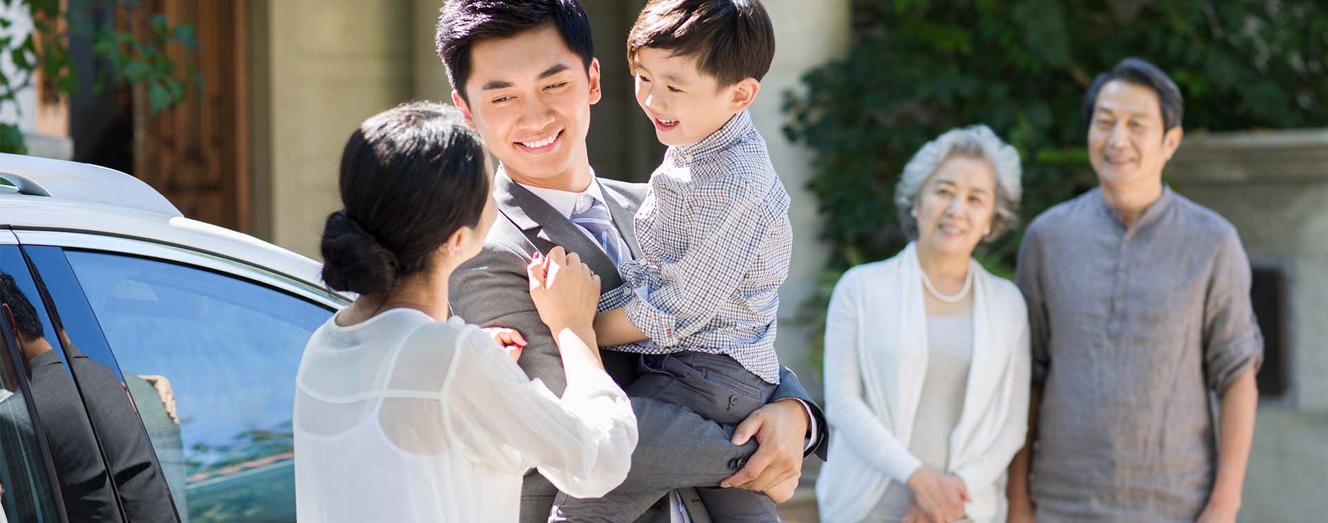 Mother and smiling father holding their child while a smiling older couple watches them in the background