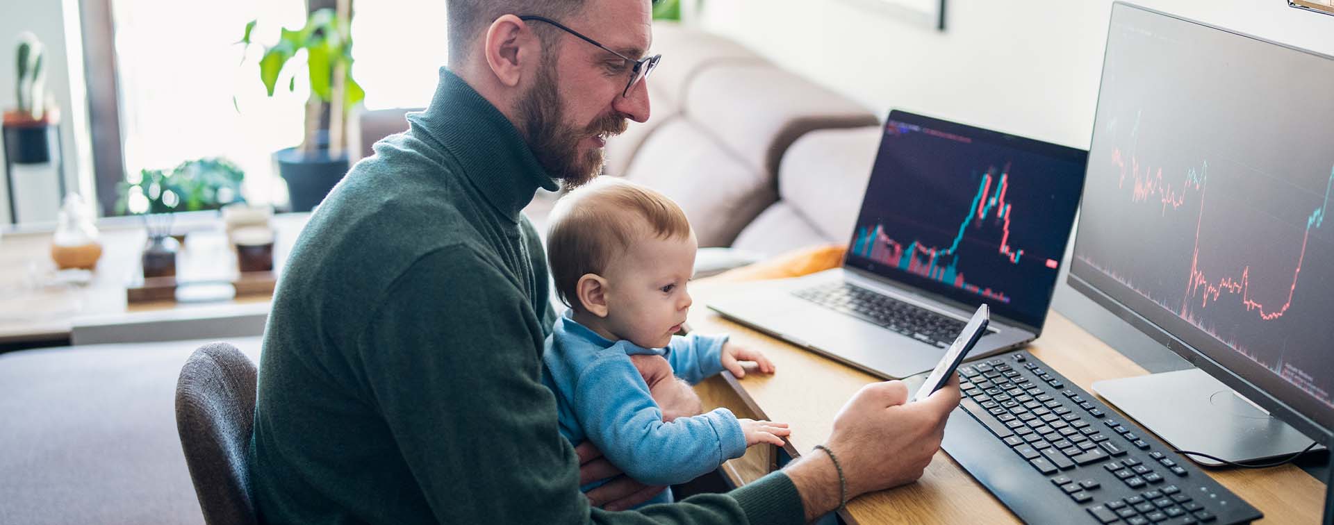 Man looking at trading app on his smart phone from home office with baby on lap