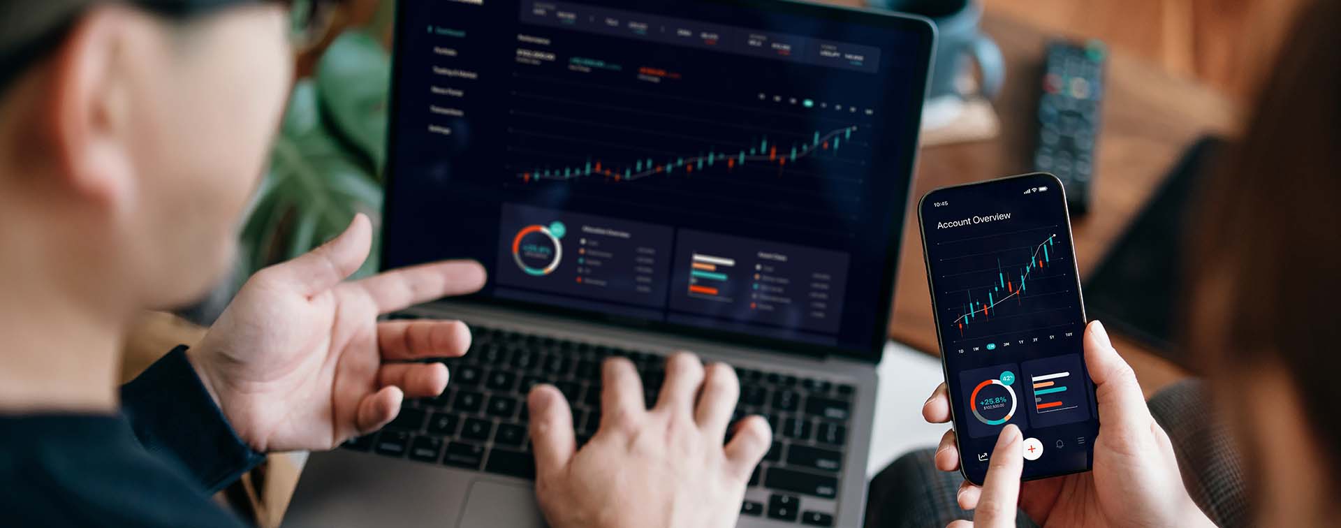 Young Asian couple managing finance and investment online, analyzing stock market trades with mobile app on laptop and smartphone. Making financial plans