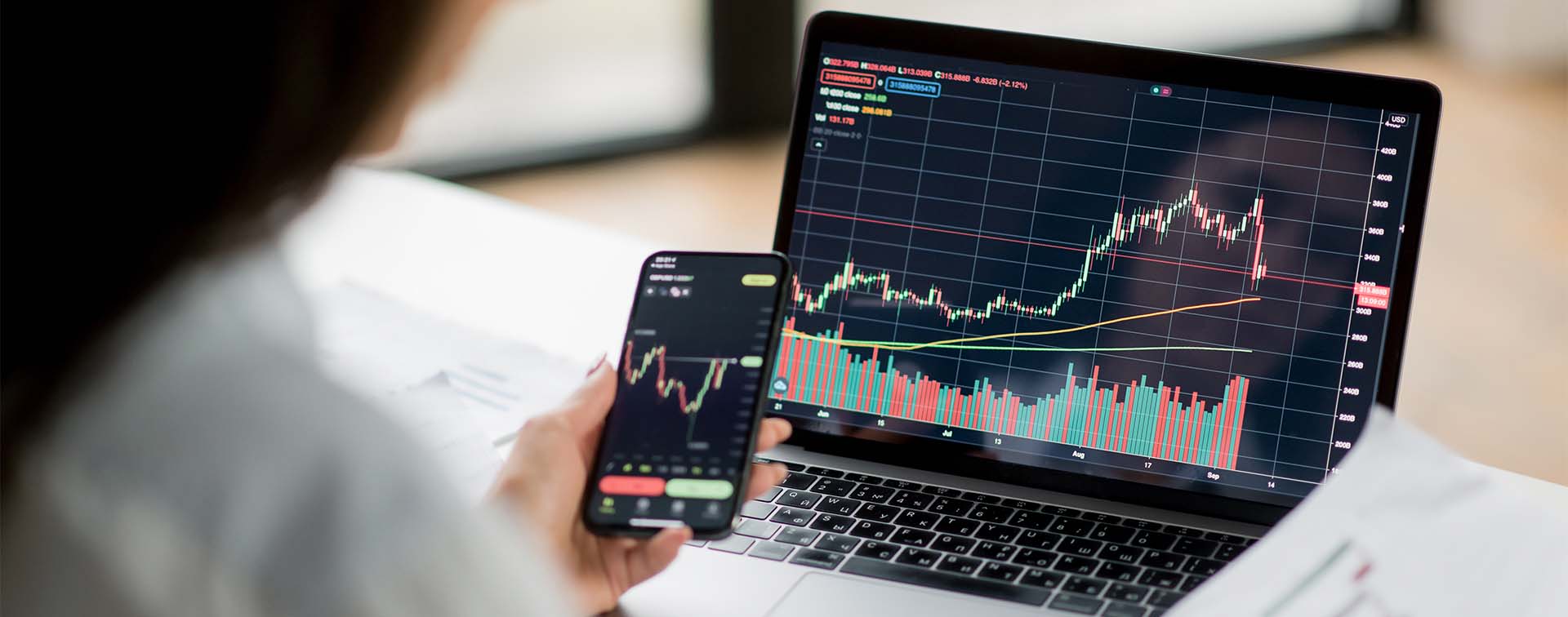 Successful Smart female crypto investor analyzing charts on laptop and phone for trading