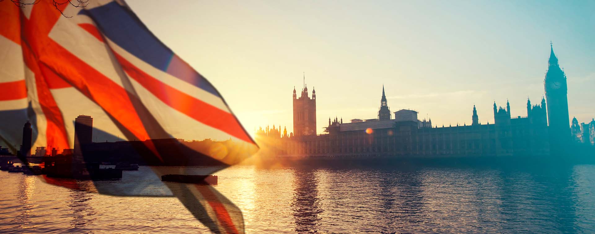 The UK flag flying in front of the London skyline at sunrise