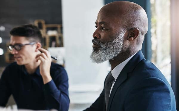 A businessman looking ahead with another man in the background holding a pen