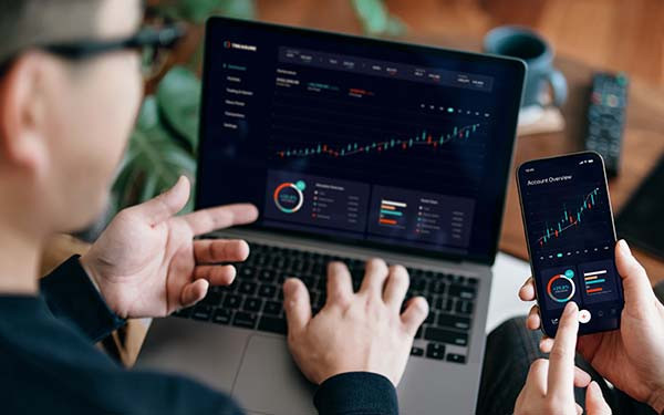 Young Asian couple managing finance and investment online, analyzing stock market trades with mobile app on laptop and smartphone. Making financial plans