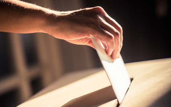 Hand posting a ballot into a ballot box