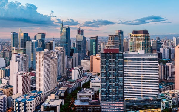 Manila’s skyline filled with tall buildings, cast in pink light by sunset, with clouds in the background