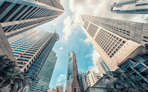Several towering city buildings in Singapore seen from ground level looking up, with the blue sky and clouds above
