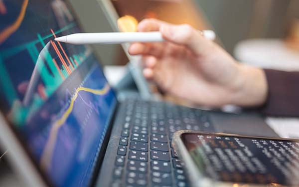 Person pointing with a stylus to charts on a laptop screen