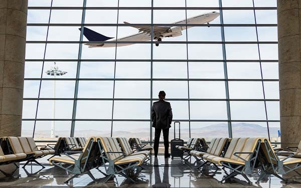 Businessman with luggage waiting in the airport looking out window as plane takes off
